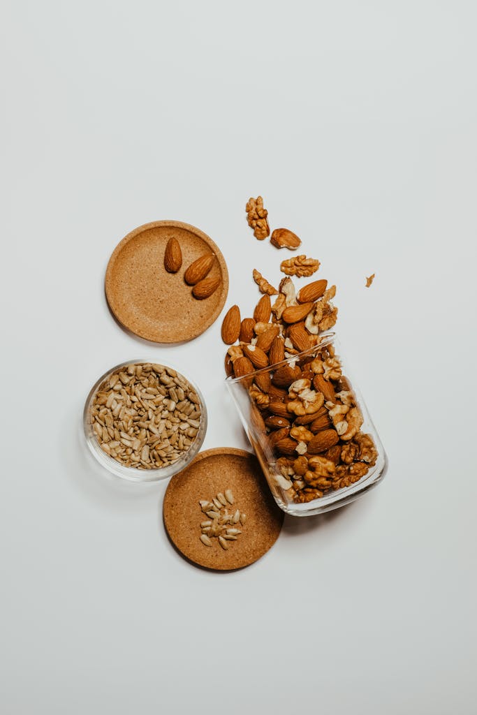 best healthy snacks at whole foods market: A flat-lay of mixed almonds, walnuts, and sunflower seeds in glass jars over a white surface.