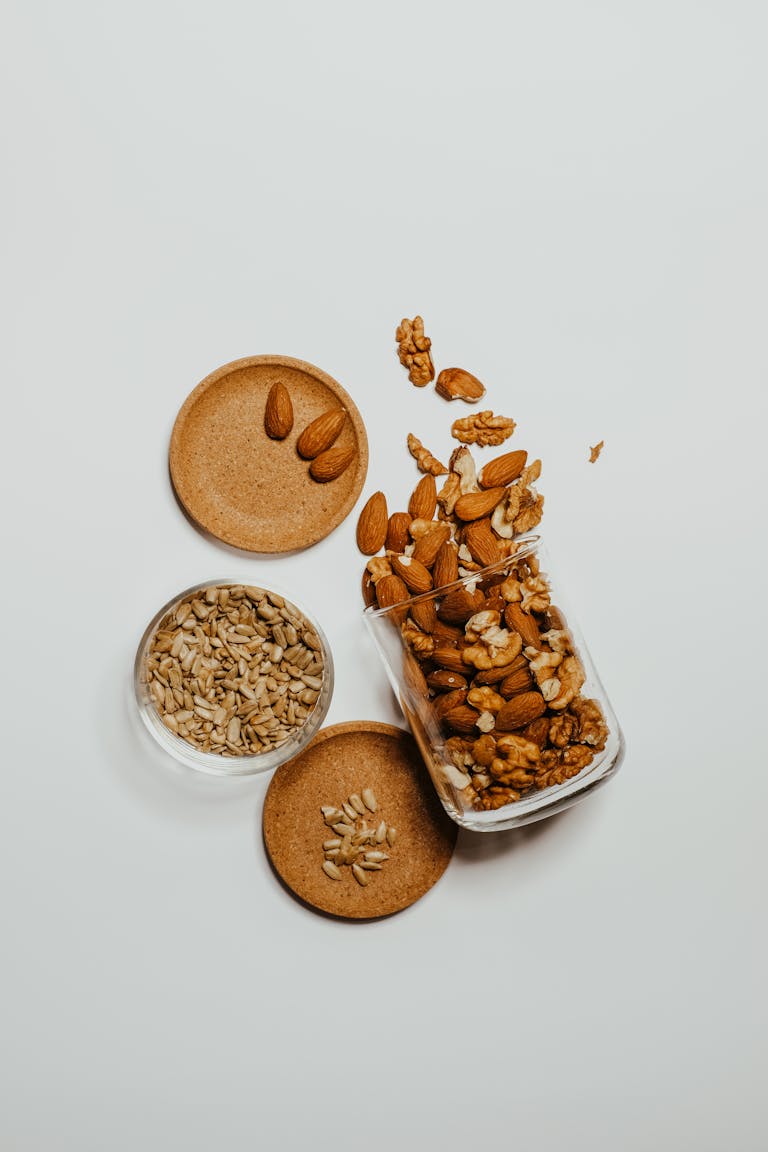 best healthy snacks at whole foods market: A flat-lay of mixed almonds, walnuts, and sunflower seeds in glass jars over a white surface.