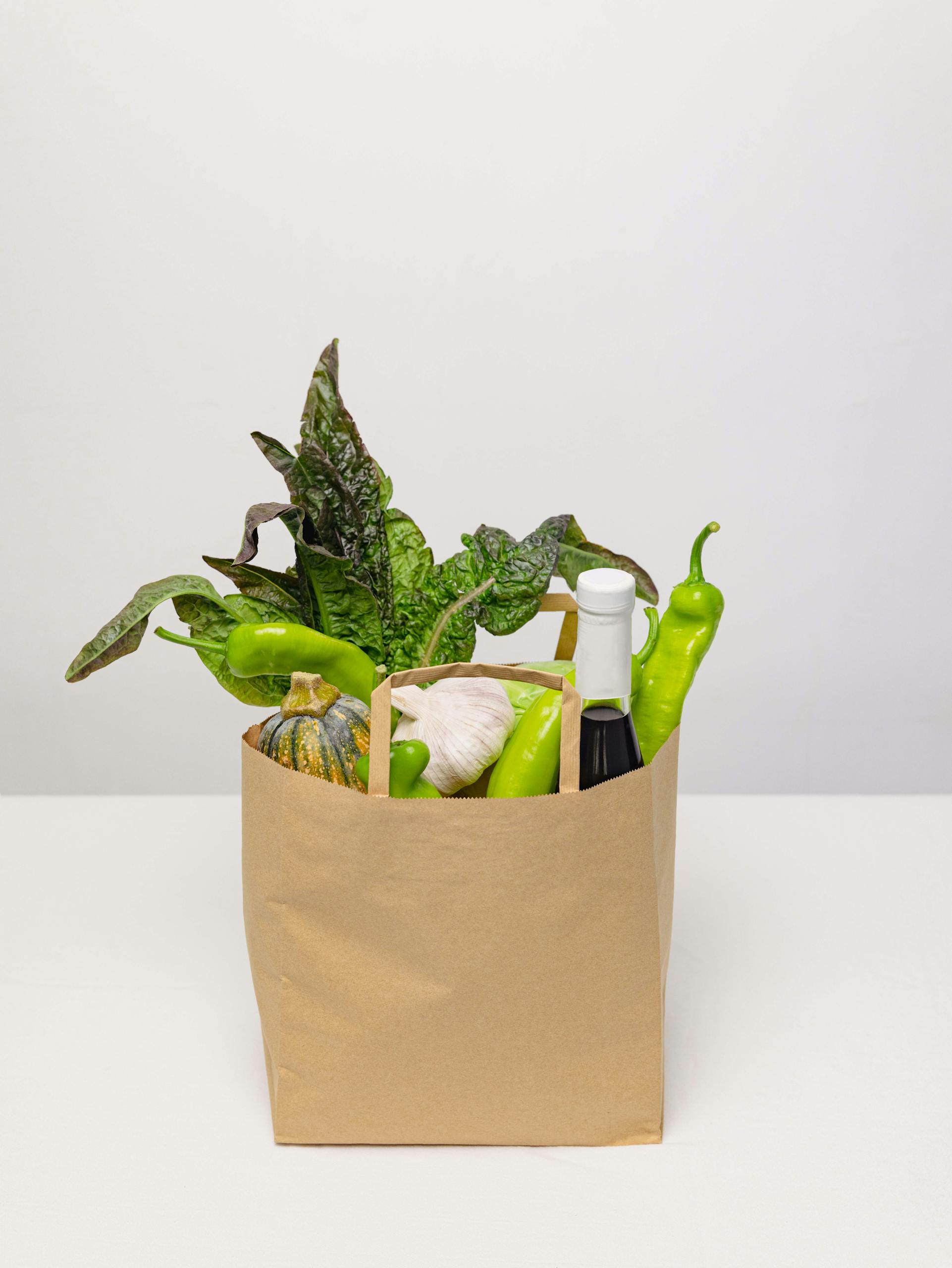 How to Shop Healthy on a Budget: A kraft paper bag filled with fresh vegetables and a bottle, against a plain background.