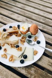 high-protein snacks: A rustic breakfast plate with cheese, walnuts, eggs, and blueberries on a wooden table.