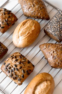 fibermaxxing: A variety of artisan breads with seeds cooling on a wire rack, showcasing rich textures and grains.