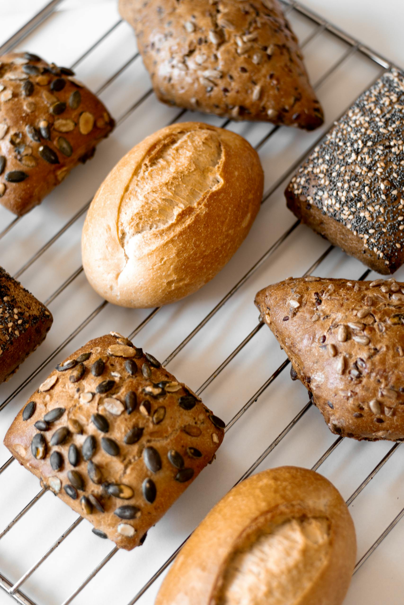 fibermaxxing: A variety of artisan breads with seeds cooling on a wire rack, showcasing rich textures and grains.