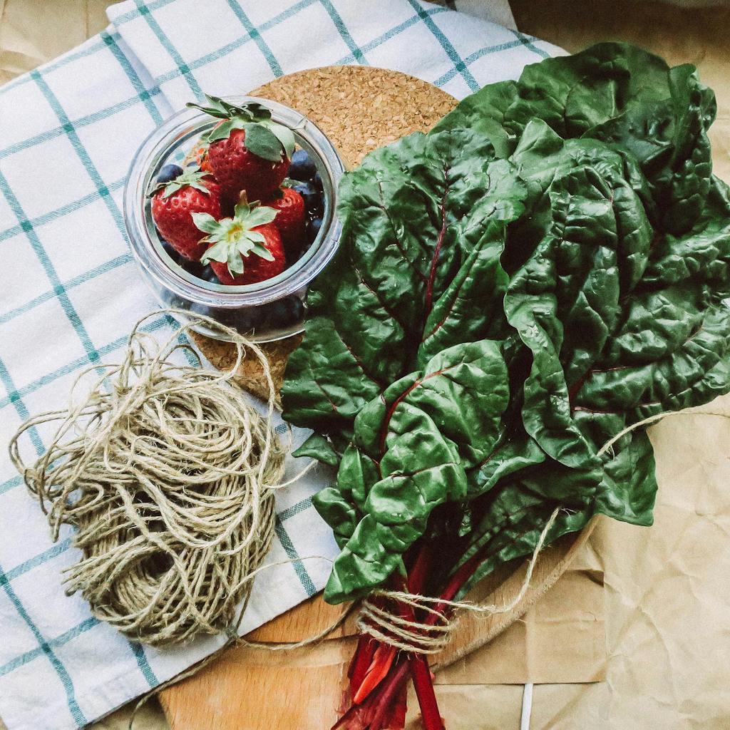Swiss chard benefits: A vibrant flat lay of Swiss chard with fresh strawberries and blueberries on a checkered cloth.