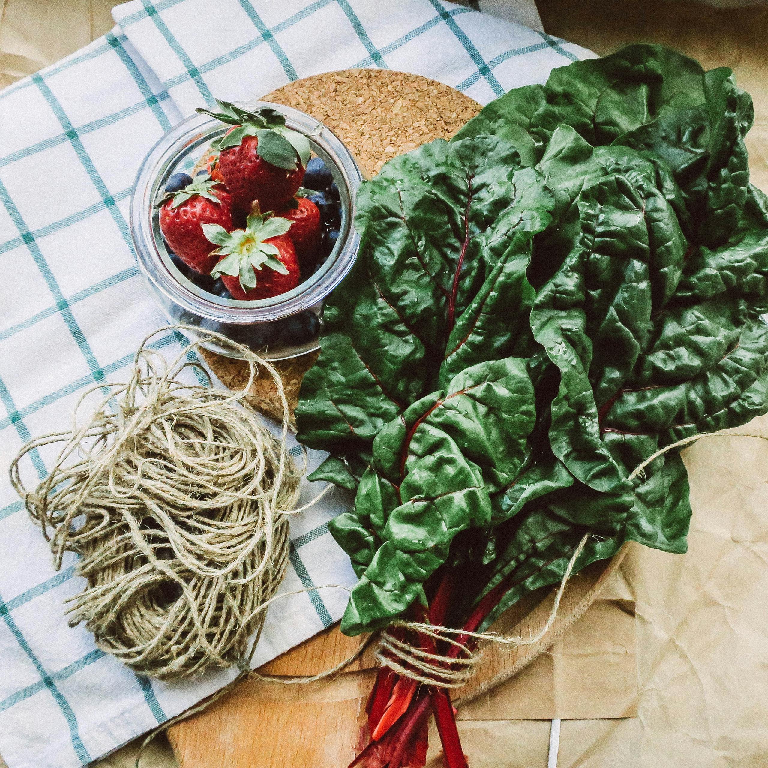 Swiss chard benefits: A vibrant flat lay of Swiss chard with fresh strawberries and blueberries on a checkered cloth.