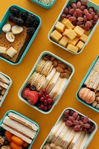 Best Post-Workout Meals for Muscle Recovery: Assorted lunch boxes with snacks, fruits, and cheese on a vibrant yellow background.