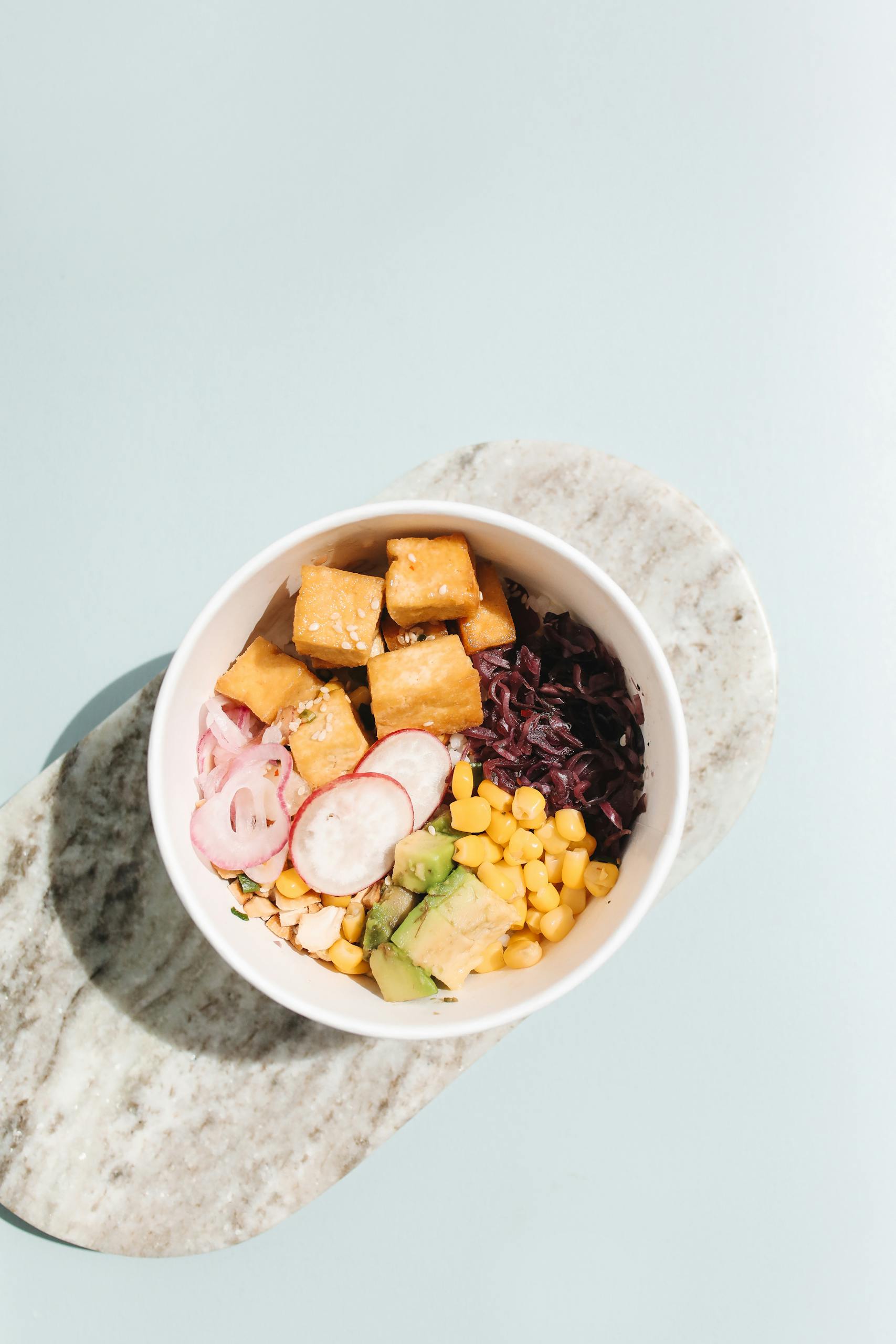 what does a balanced meal look like: Bright and healthy tofu poke bowl with fresh ingredients on a marble surface.