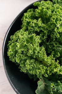 spinach vs kale nutrition: Close-up of curly kale leaves in a black ceramic bowl on marble surface. Ideal for healthy eating concepts.