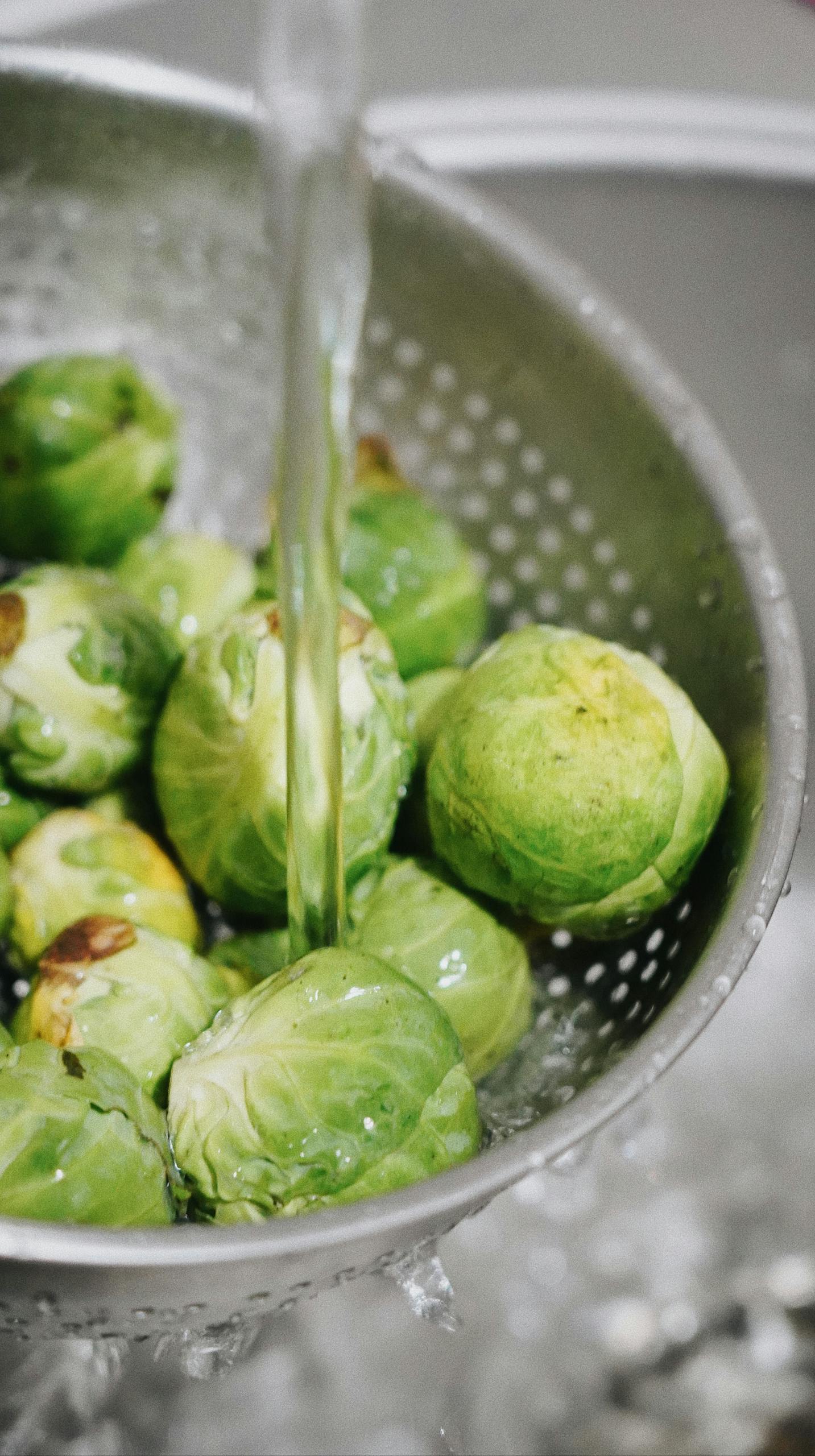 best foods for longevity: Close-up of fresh Brussels sprouts being washed in a strainer, emphasizing healthy food preparation.