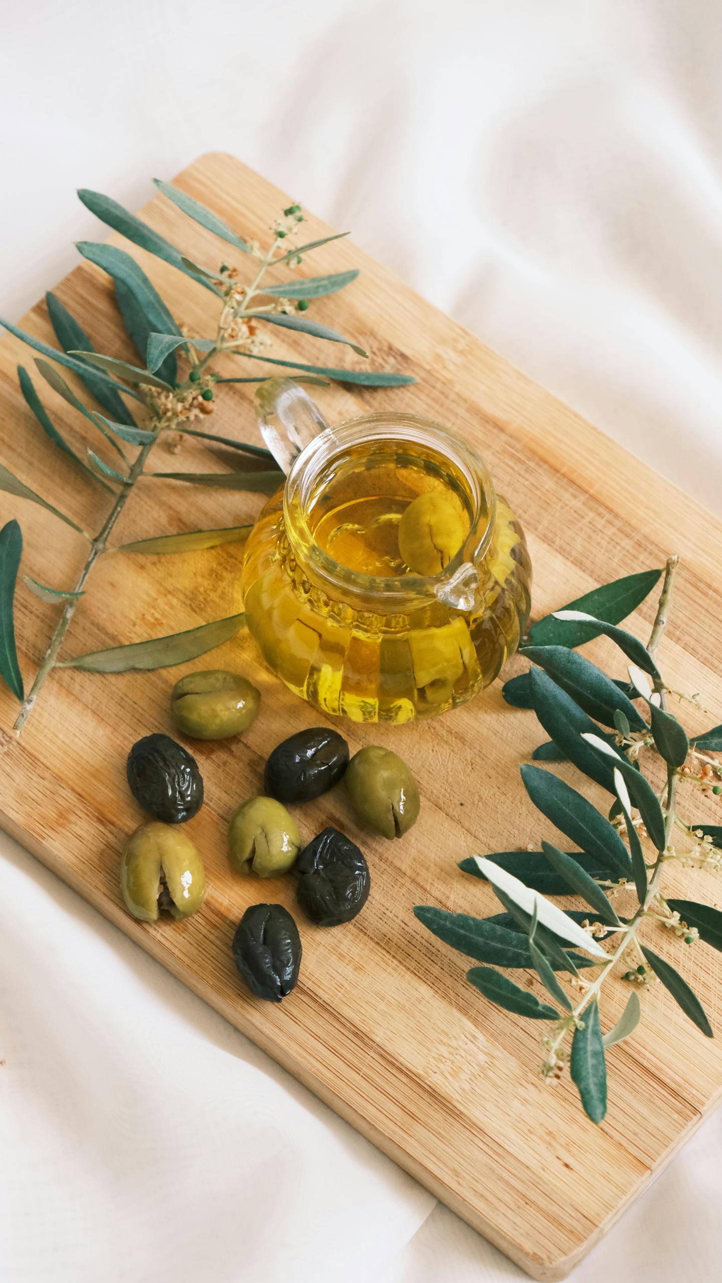 best foods to reduce brain fog: Cozy setup featuring olives and olive oil on a wooden board with olive branches.