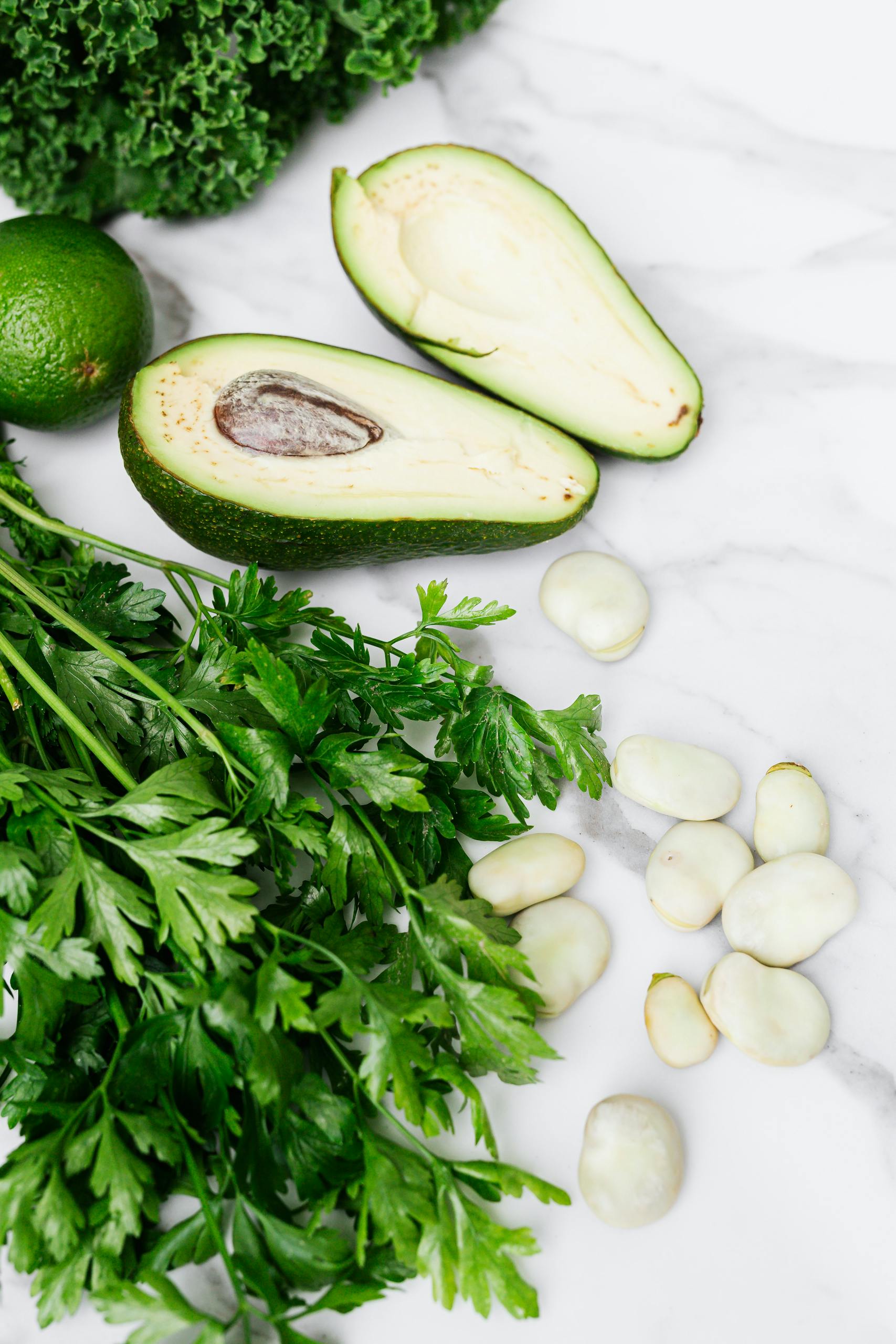 Volume Eating for Weight Loss: Crisp parsley, ripe avocado, broad beans, and lime on a white marble surface, a fresh culinary display.