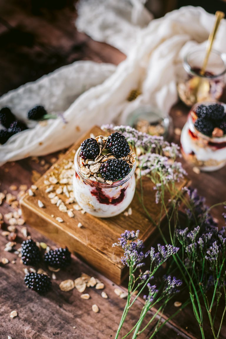 Greek yogurt vs. regular yogurt: Delicious blackberry yogurt parfait with granola and flowers in a rustic setting.