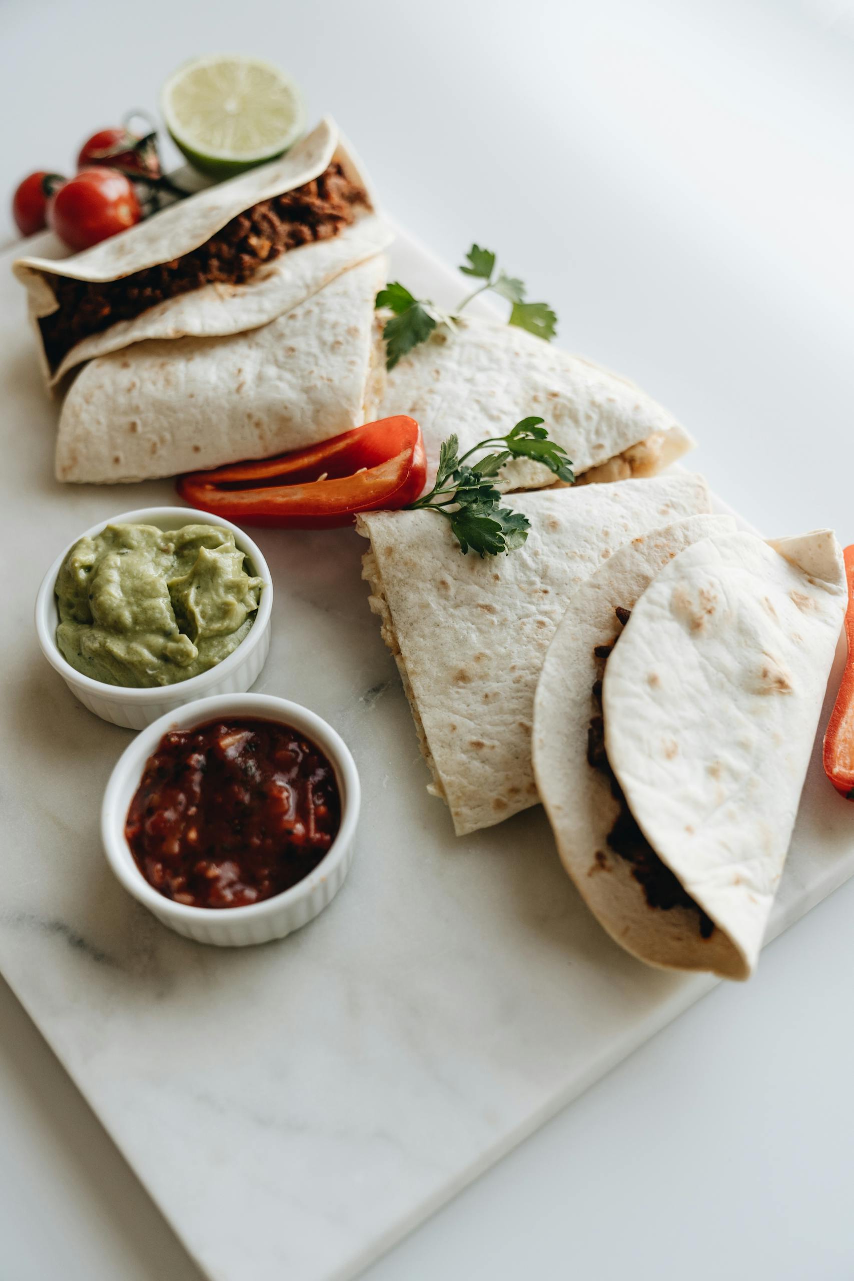 Corn Tortillas vs. Flour Tortillas: Delicious quesadillas served with guacamole and salsa on a marble board, perfect for lunch.