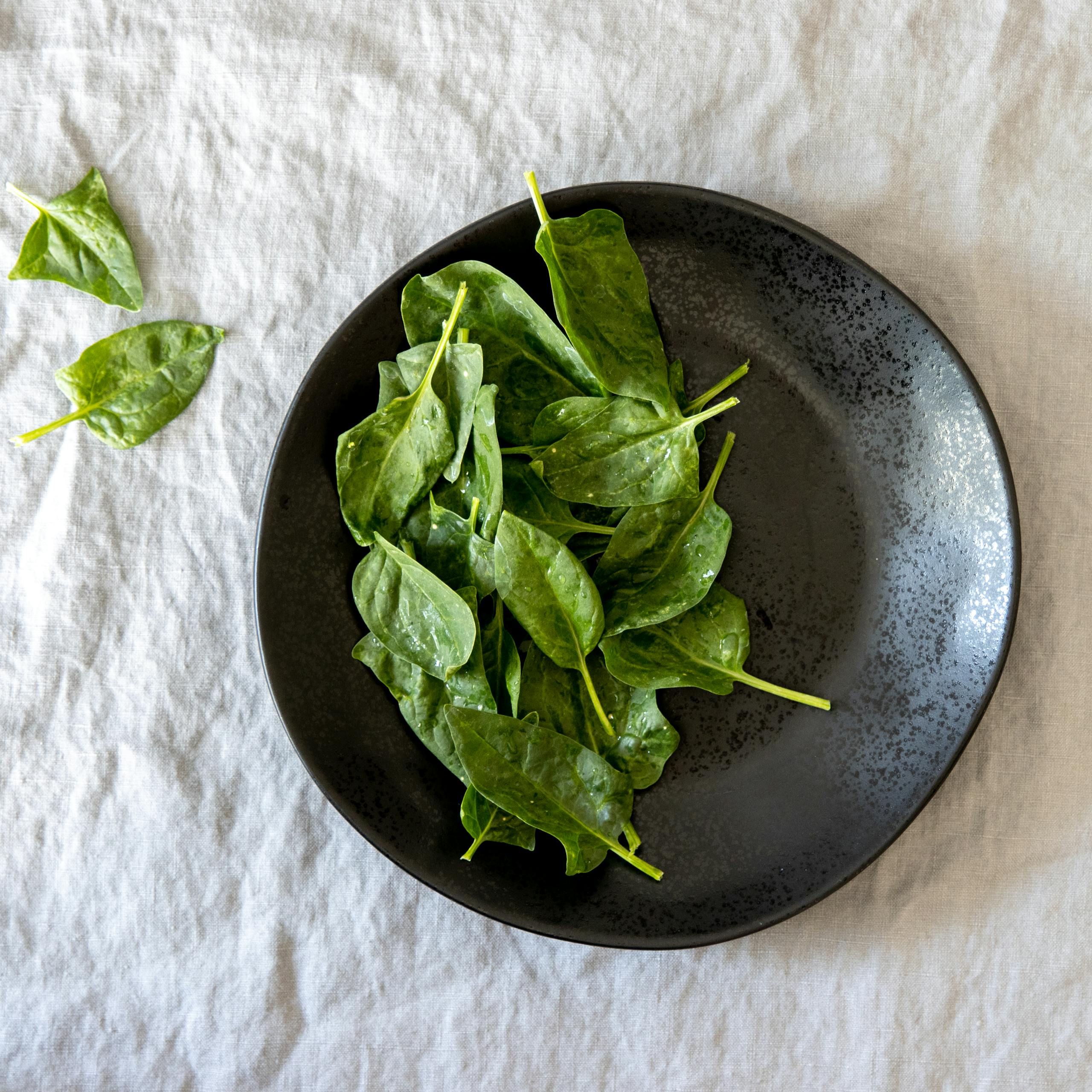 spinach vs kale nutrition: Fresh spinach leaves elegantly arranged on a rustic black plate for a healthy meal display.