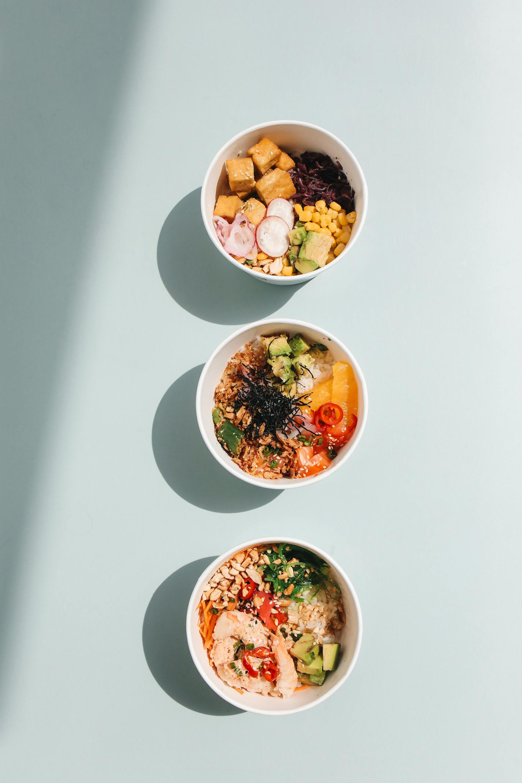 what does a balanced meal look like: Overhead view of three vibrant Hawaiian poke bowls with diverse toppings in natural light.