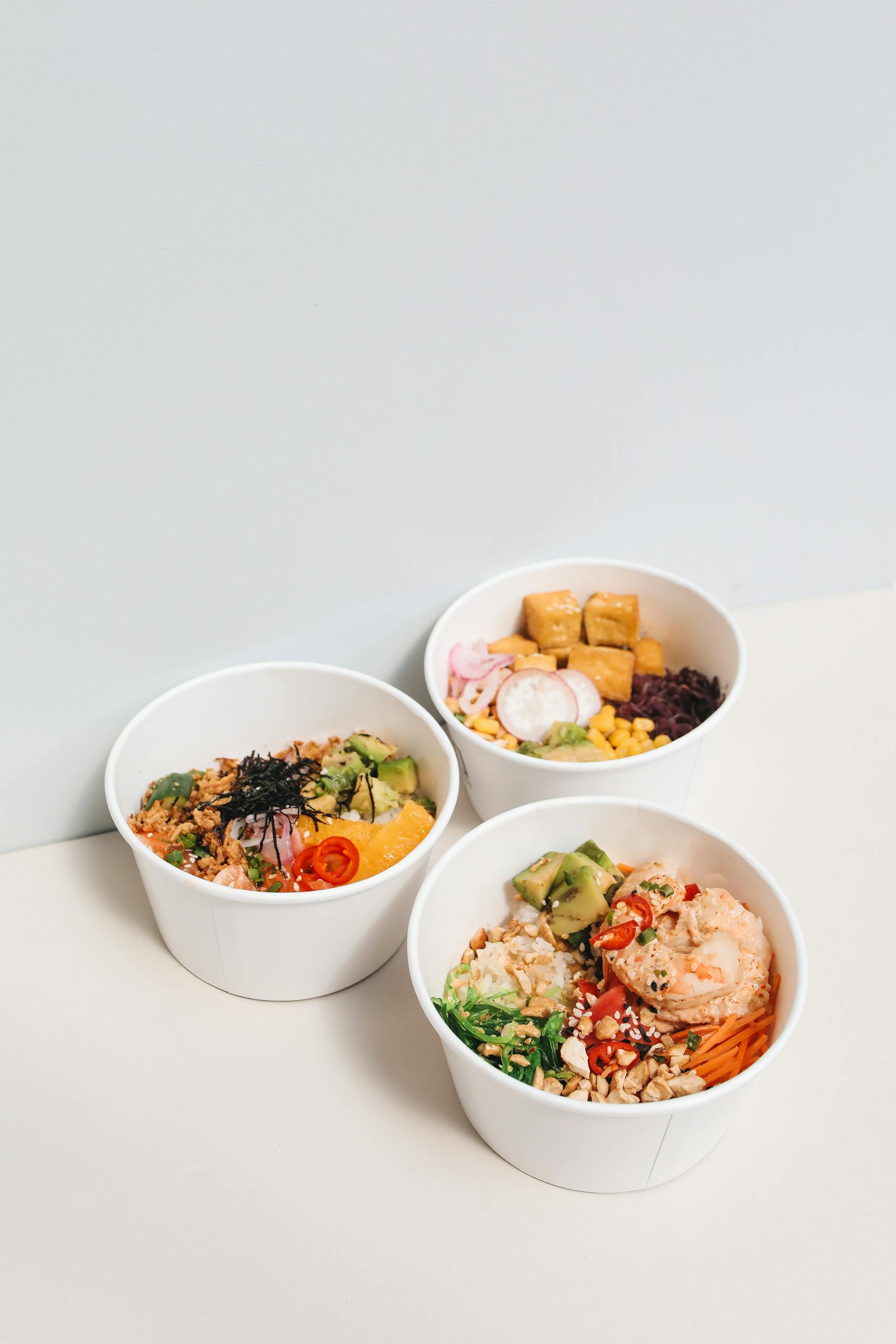 what does a balanced meal look like: Three delicious healthy poke bowls with fresh ingredients on a white surface, perfect for food photography.
