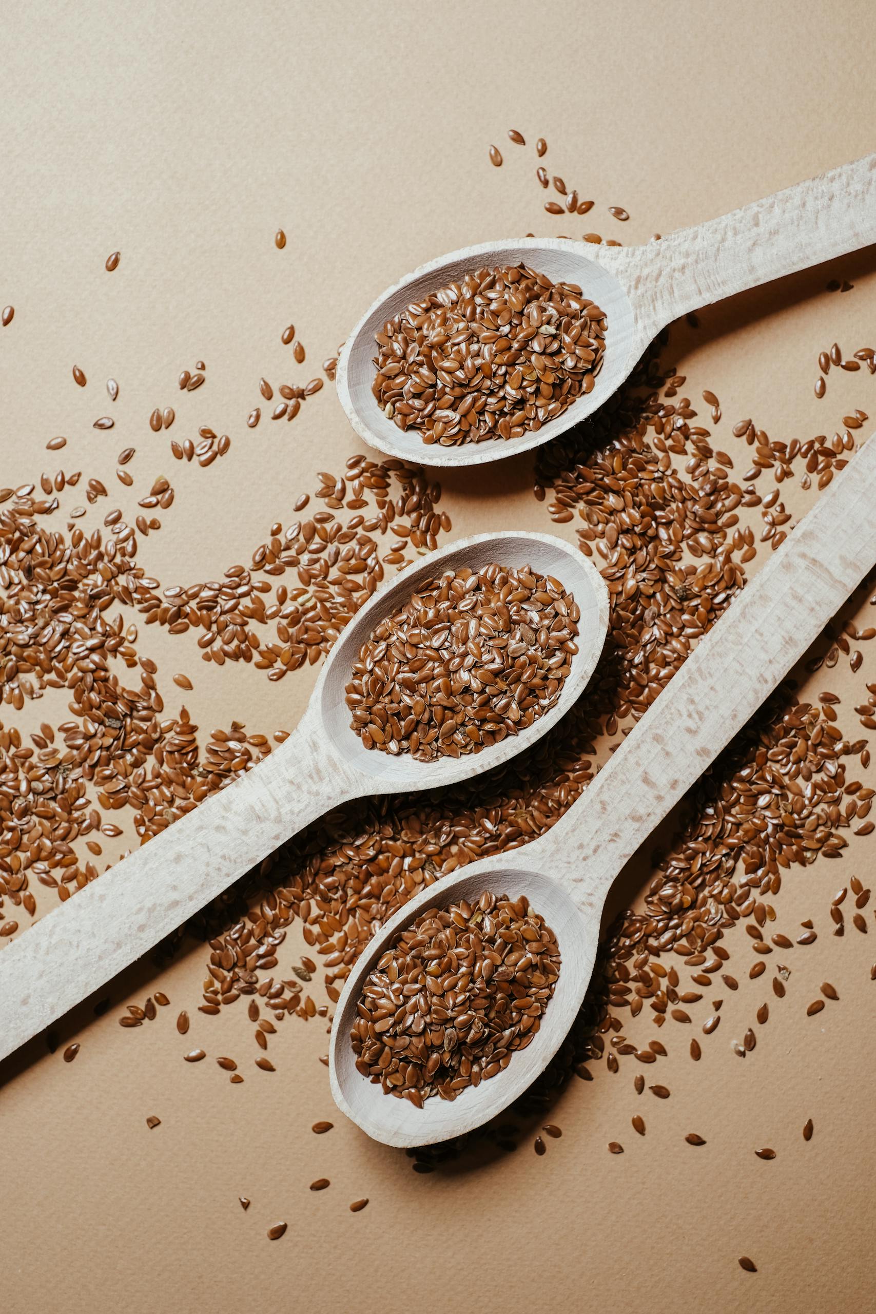 seed cycling for hormones: Three wooden spoons with flax seeds on a textured surface highlighting natural health food.