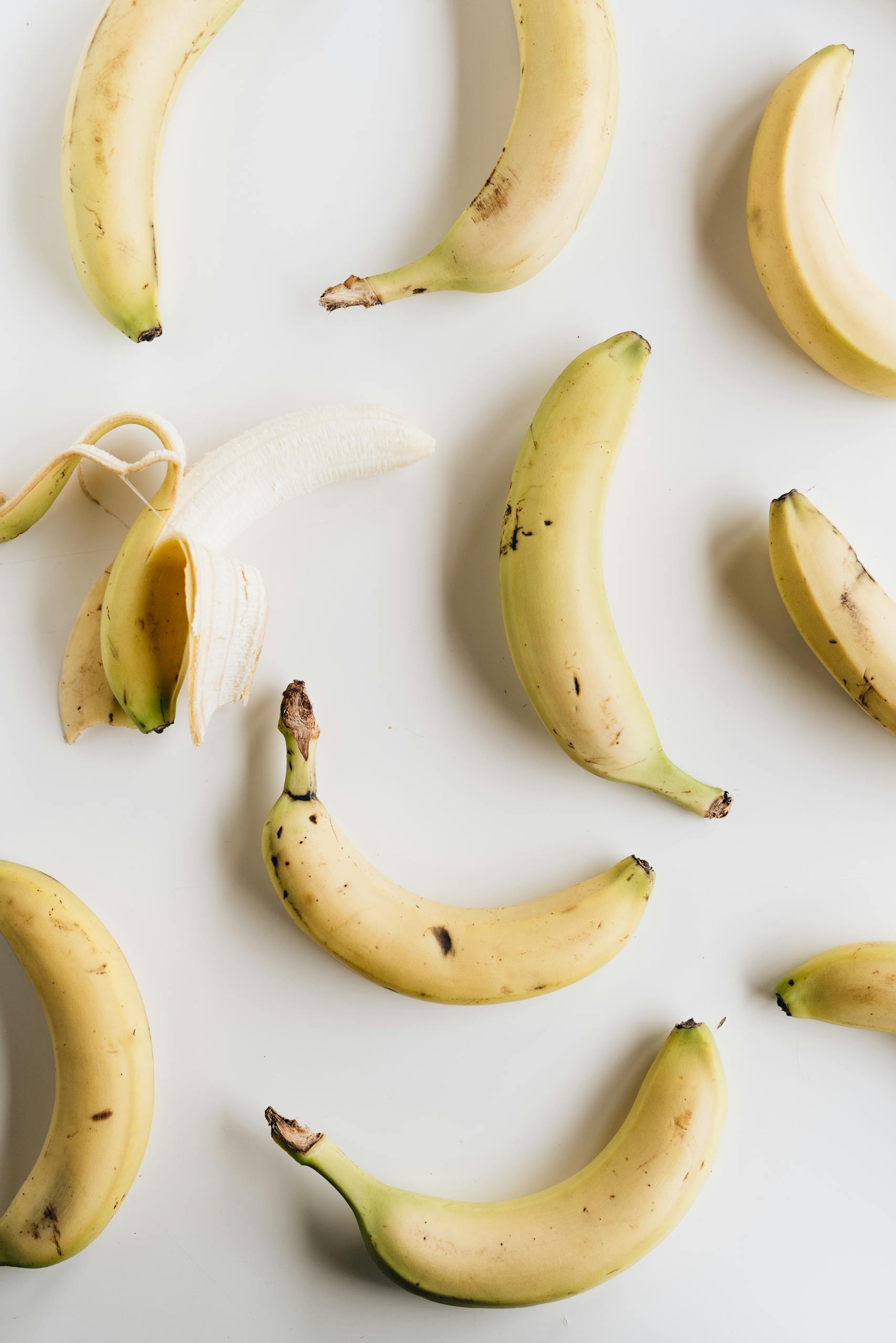 potassium-rich foods for blood pressure: Top view composition of ripe half peeled banana among fresh yellow unpeeled bananas placed on white background under bright light