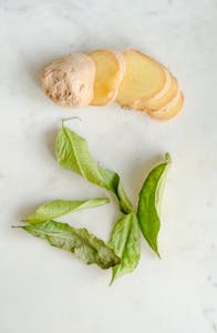 Plant-Based Foods for Joint Support: Top view of fresh ginger slices paired with green leaves, creating a natural vibe on a white background.