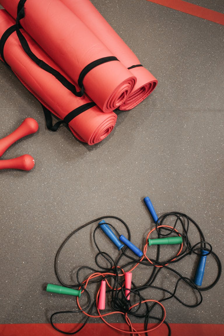 fasted cardio for fat loss: Top view of red yoga mats, jump ropes, and dumbbells on gym floor.