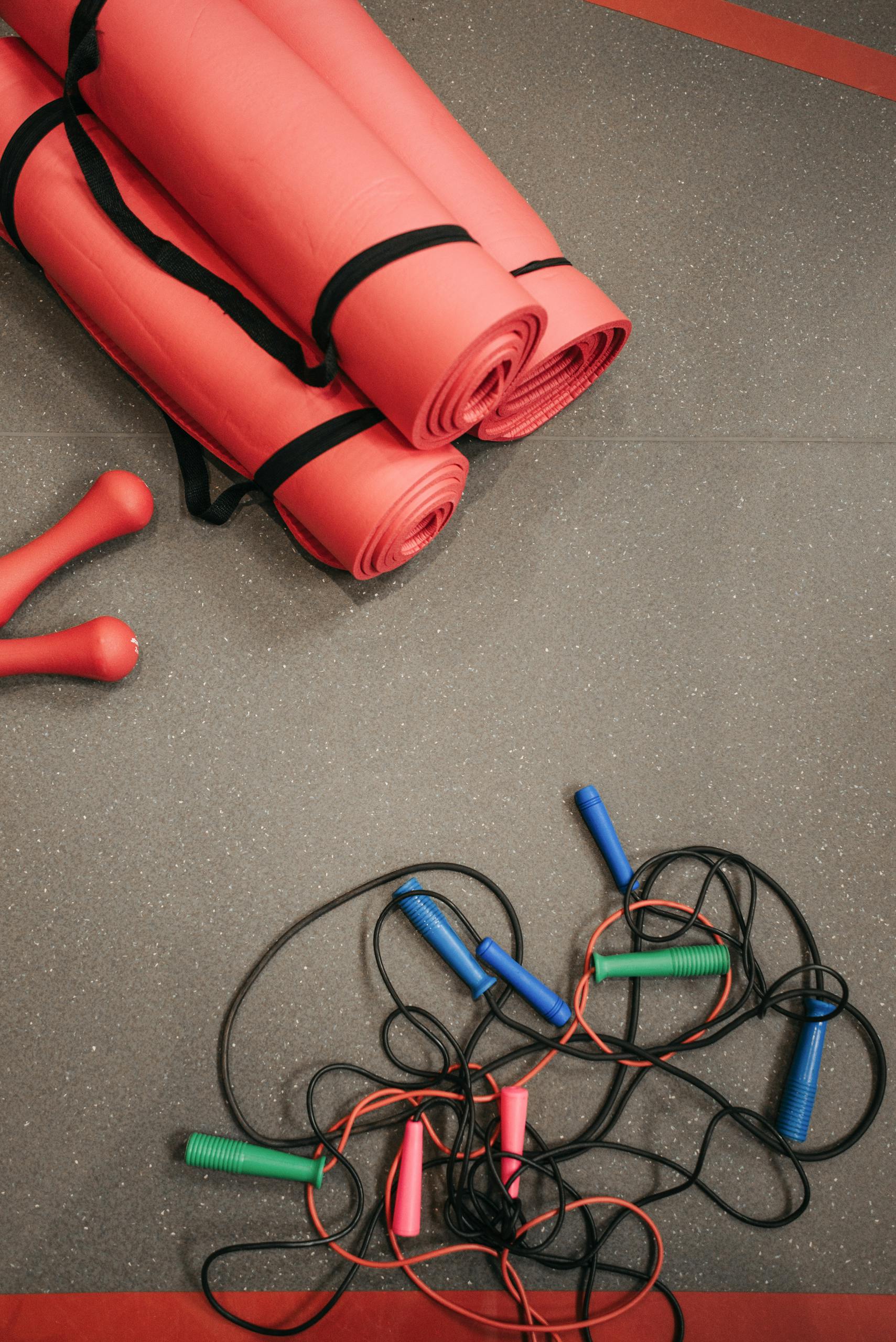 fasted cardio for fat loss: Top view of red yoga mats, jump ropes, and dumbbells on gym floor.