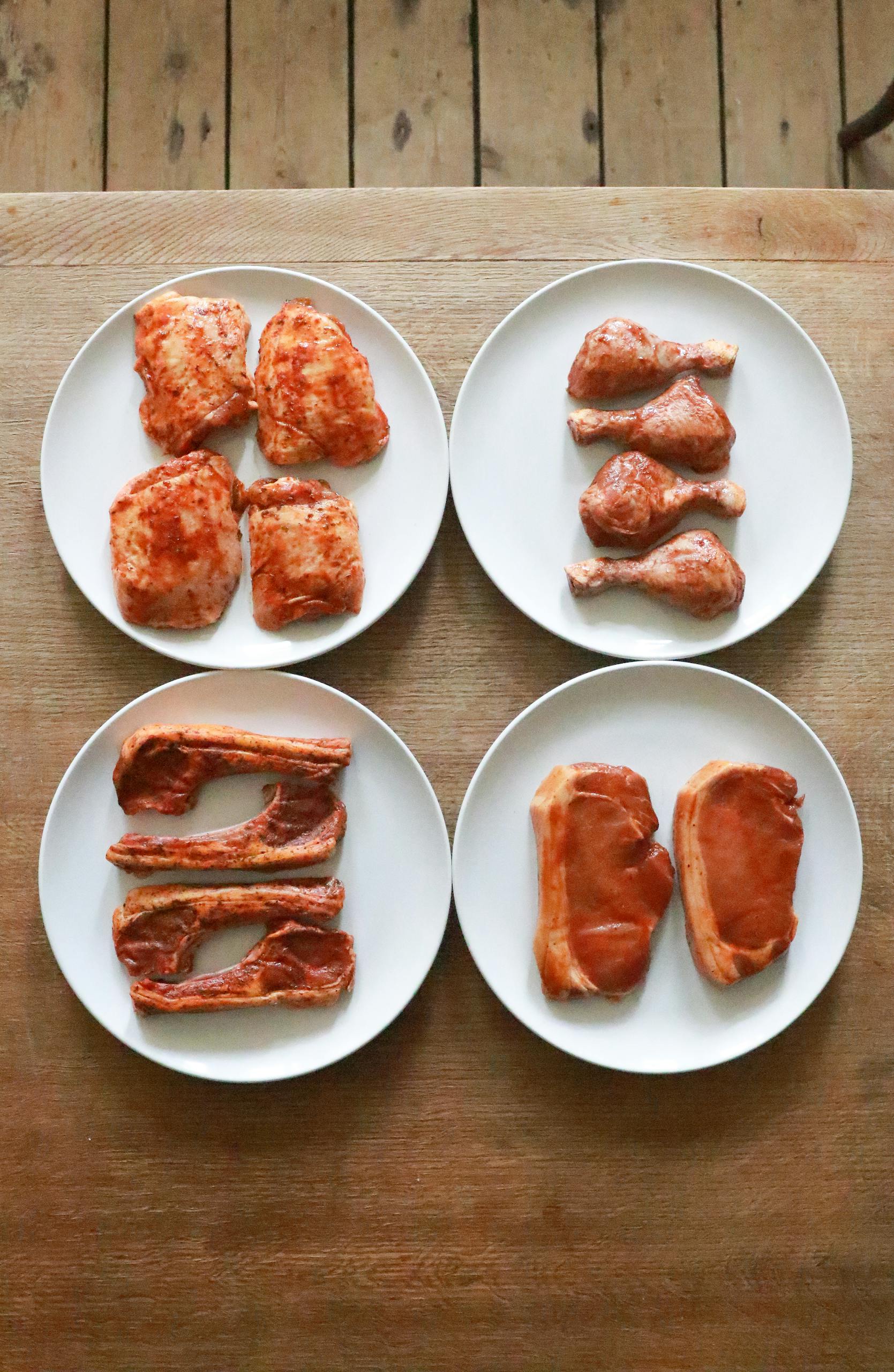 fad diets to avoid: Top view of uncooked different meat fillet and steaks with drumsticks and ribs with seasoning on white plates placed on wooden table