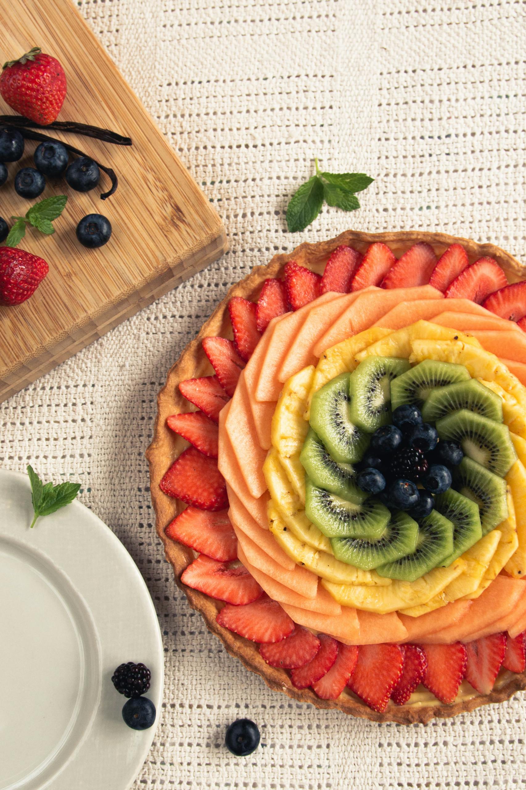 fibermaxxing: Vibrant fruit tart decorated with strawberries, kiwi, and blueberries on a table.