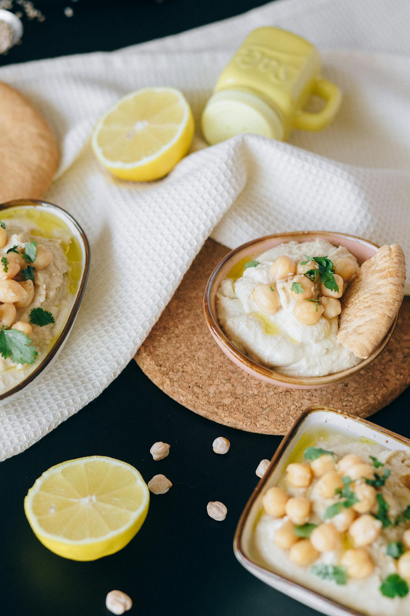 how to use nutritional yeast: A close-up of creamy hummus topped with chickpeas, lemon slices, and fresh herbs.