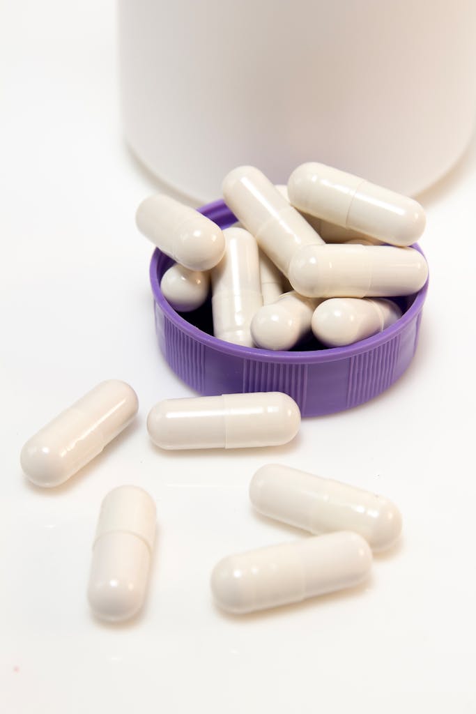 probiotic foods vs. supplements: A close-up of white capsules spilling from a container onto a purple cap, shot indoors.