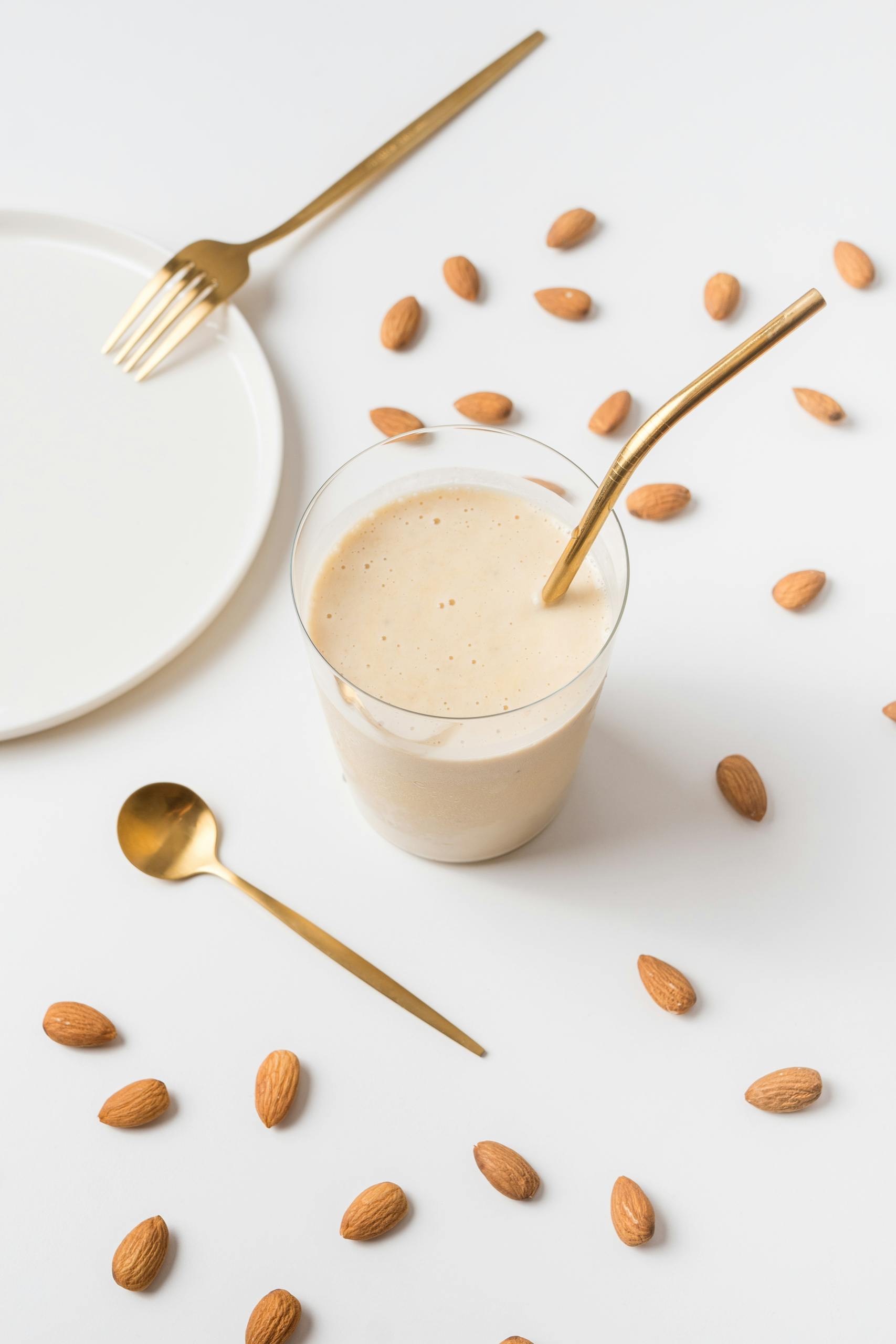 Best Post-Workout Meals for Muscle Recovery: A creamy almond smoothie on a white background, styled with golden utensils and scattered almonds.