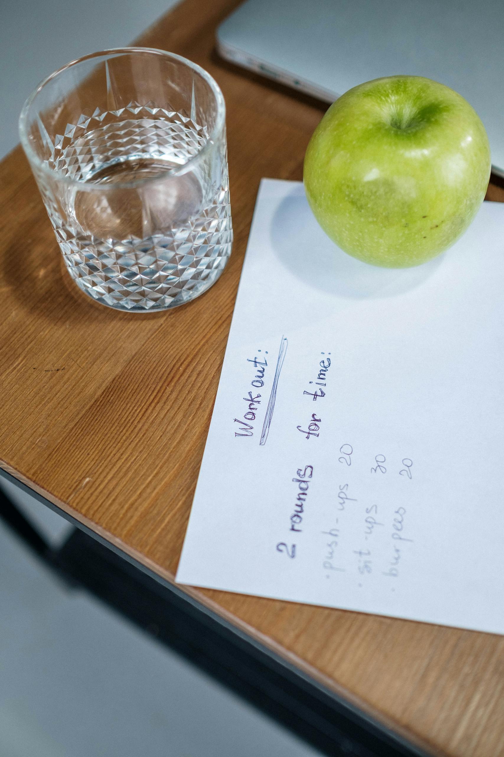 why fad diets cause weight regain: A refreshing glass of water with a green apple and workout plan on a wooden table.
