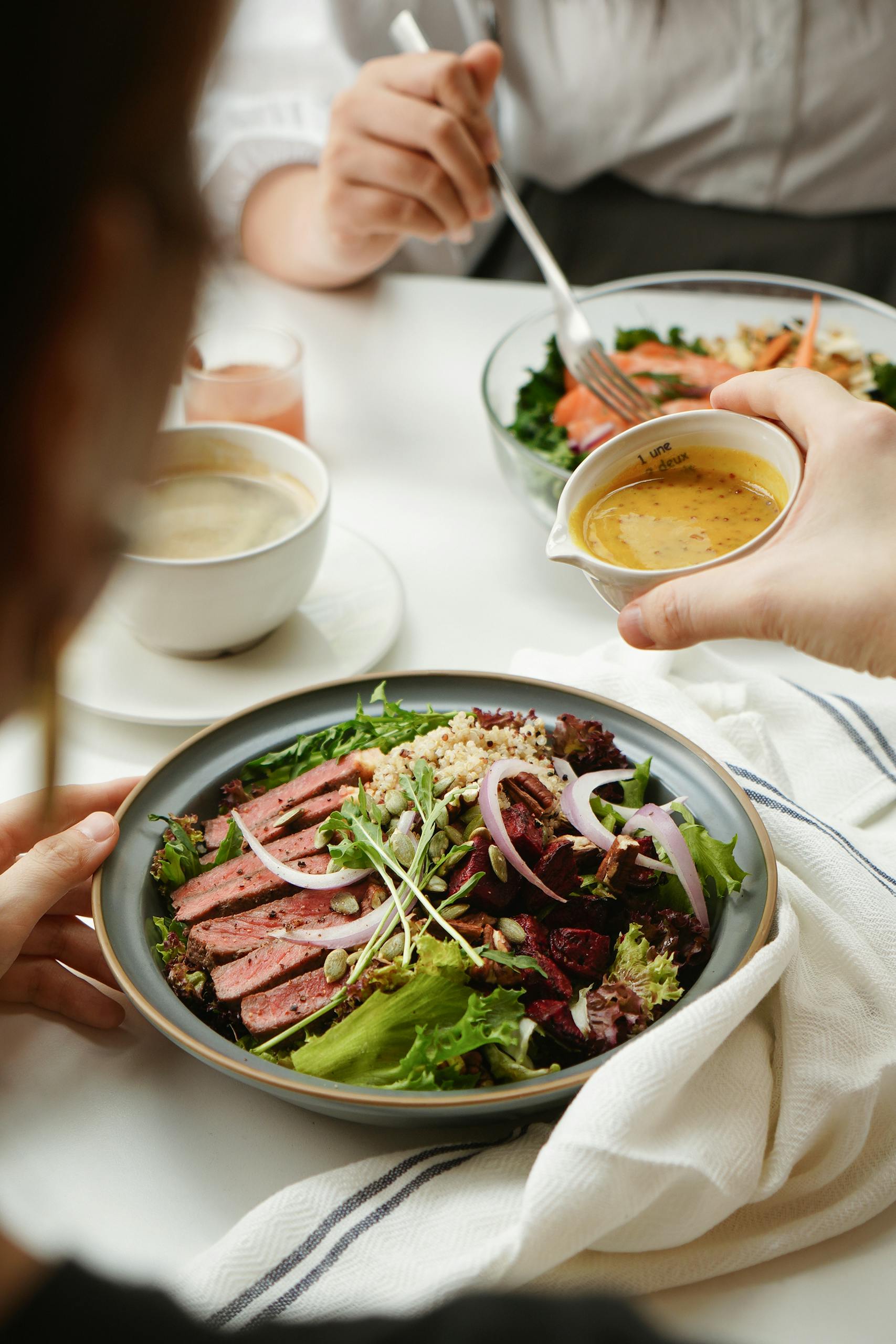 Healthiest Sweetgreen Orders: A stylish lunch scene featuring a vibrant salad and hands pouring dressing at a table.