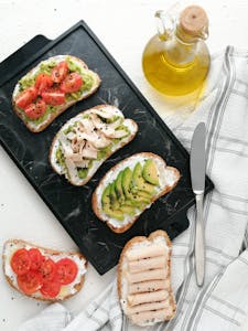 Healthy Fats for Breakfast: A top view of avocado toast varieties with fresh ingredients on a marble surface.