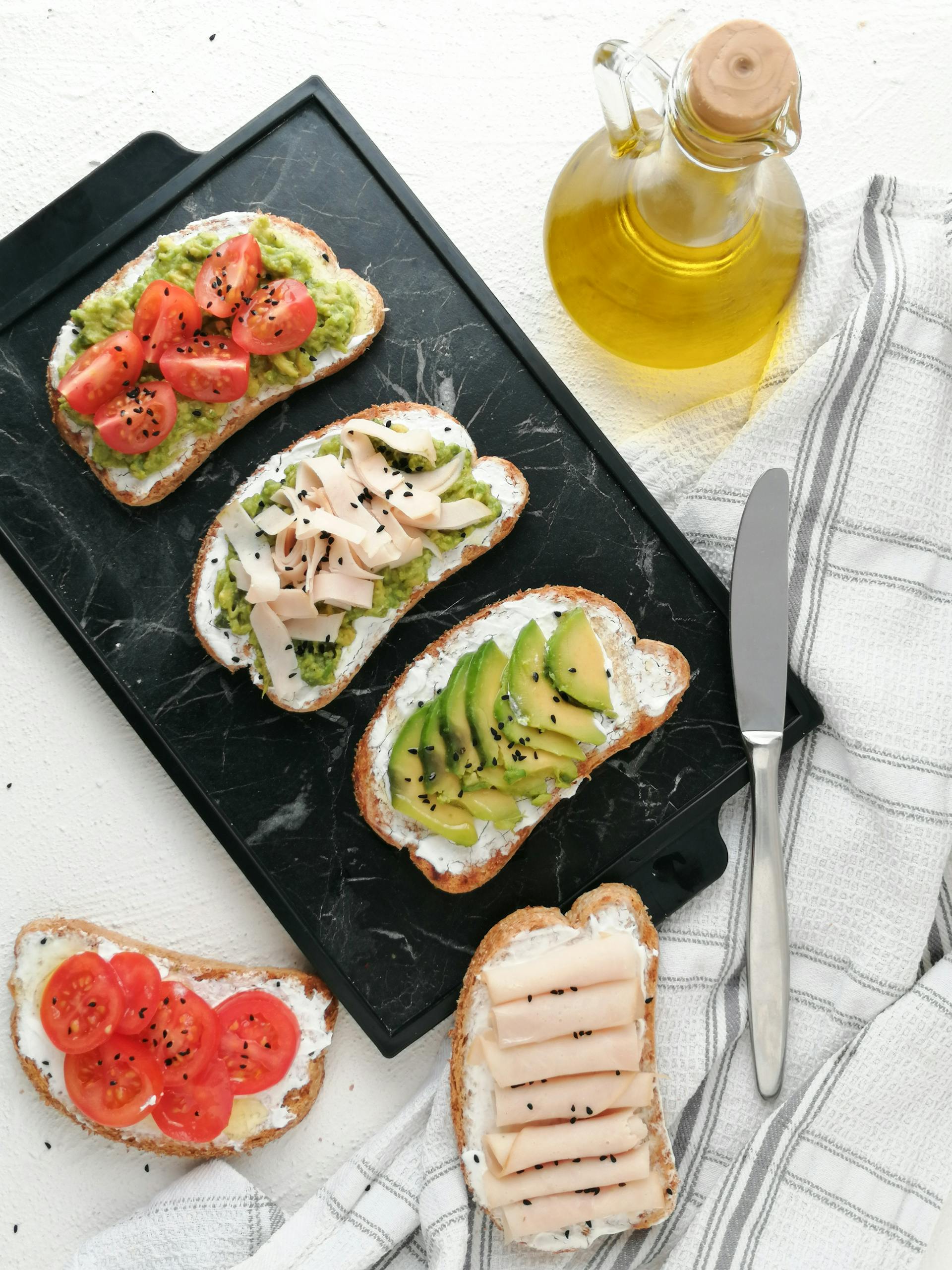 Healthy Fats for Breakfast: A top view of avocado toast varieties with fresh ingredients on a marble surface.
