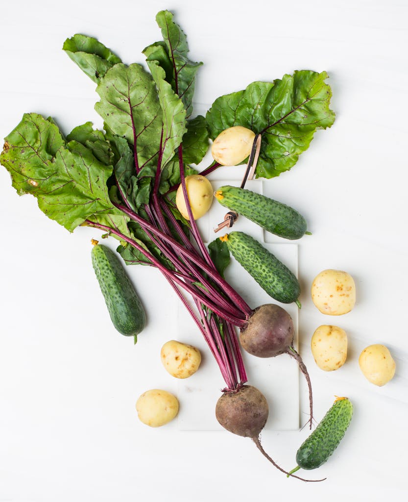 How to Make Meals Healthier: Assorted organic vegetables including beets, cucumbers, and potatoes on a white surface.