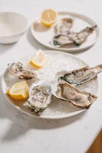 zinc and hormones: Close-up of fresh raw oysters on ice with lemon wedges on a serving plate, perfect for seafood enthusiasts.