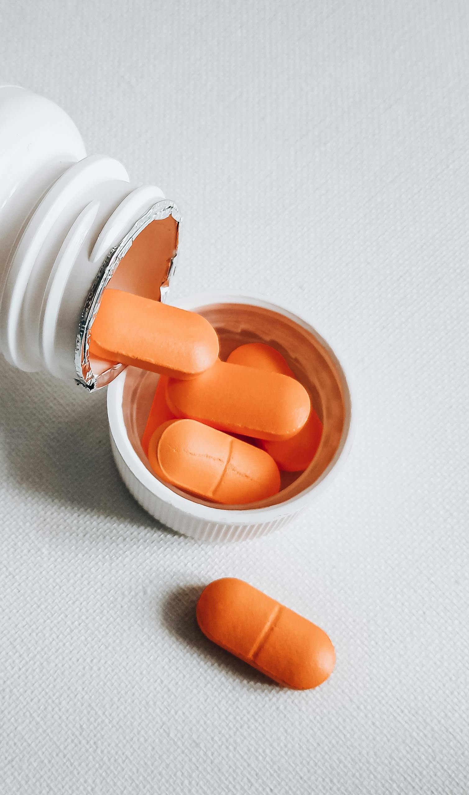 probiotic foods vs. supplements: Close-up of orange pills spilling from a white bottle on a textured surface.