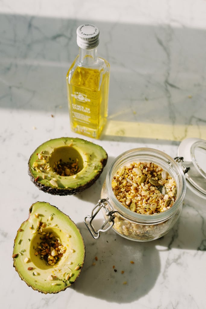 olive oil vs. avocado oil: Fresh avocado halves with pine nuts and olive oil on marble surface, highlighting healthy eating.