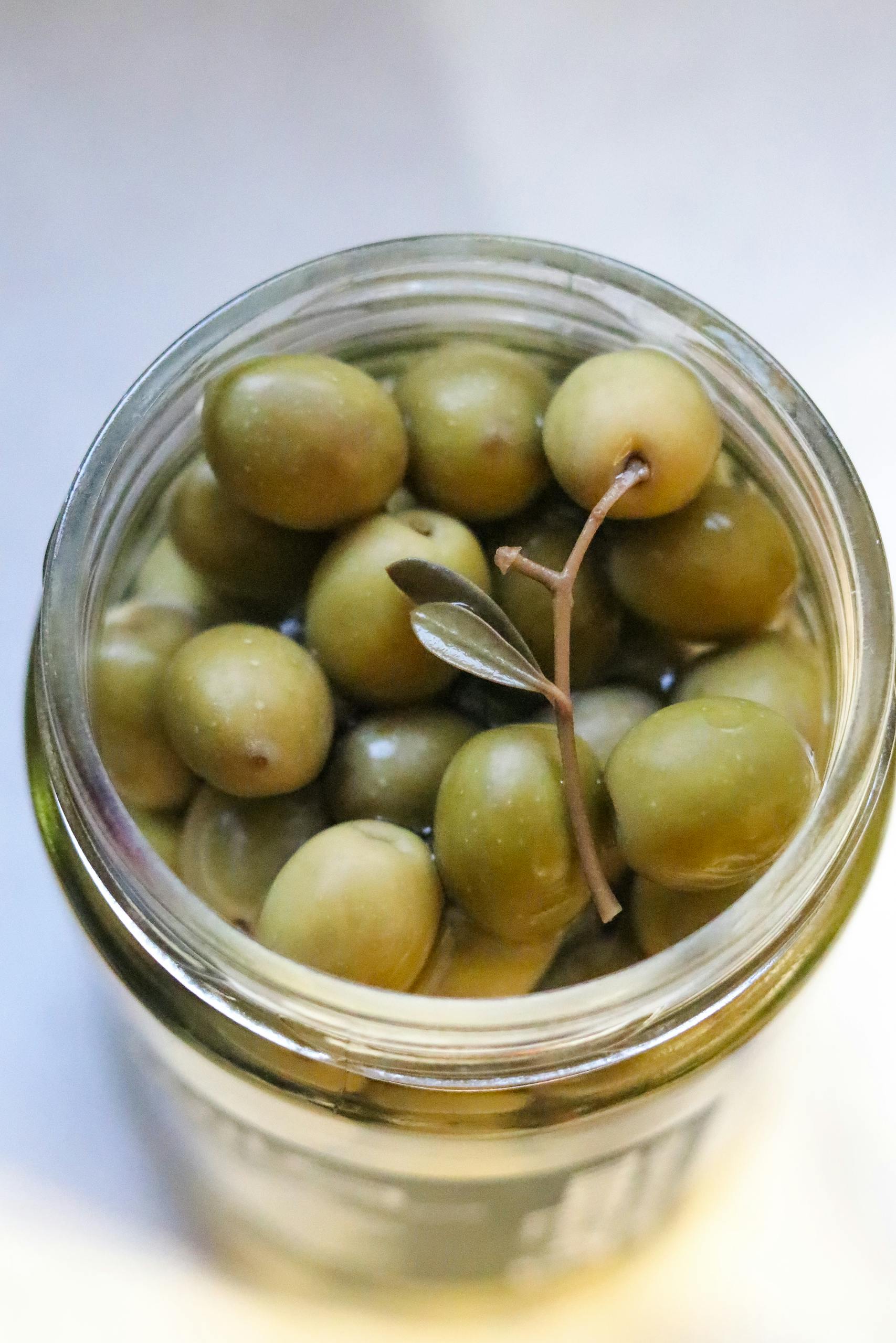 olive oil vs. avocado oil: High-angle view of green olives in a glass jar, perfect for food and culinary themes.