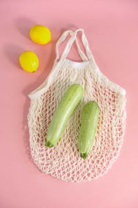 Brain-Healthy Grocery List: Top view of zucchinis and lemons in a net bag on a pink surface. Minimalist style.