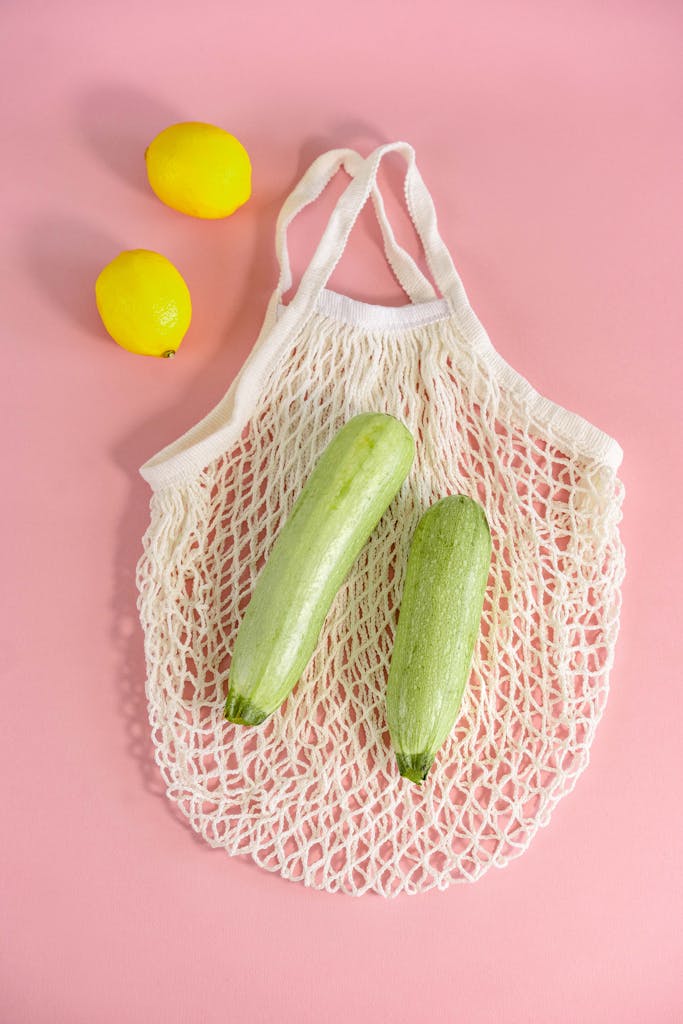 Brain-Healthy Grocery List: Top view of zucchinis and lemons in a net bag on a pink surface. Minimalist style.