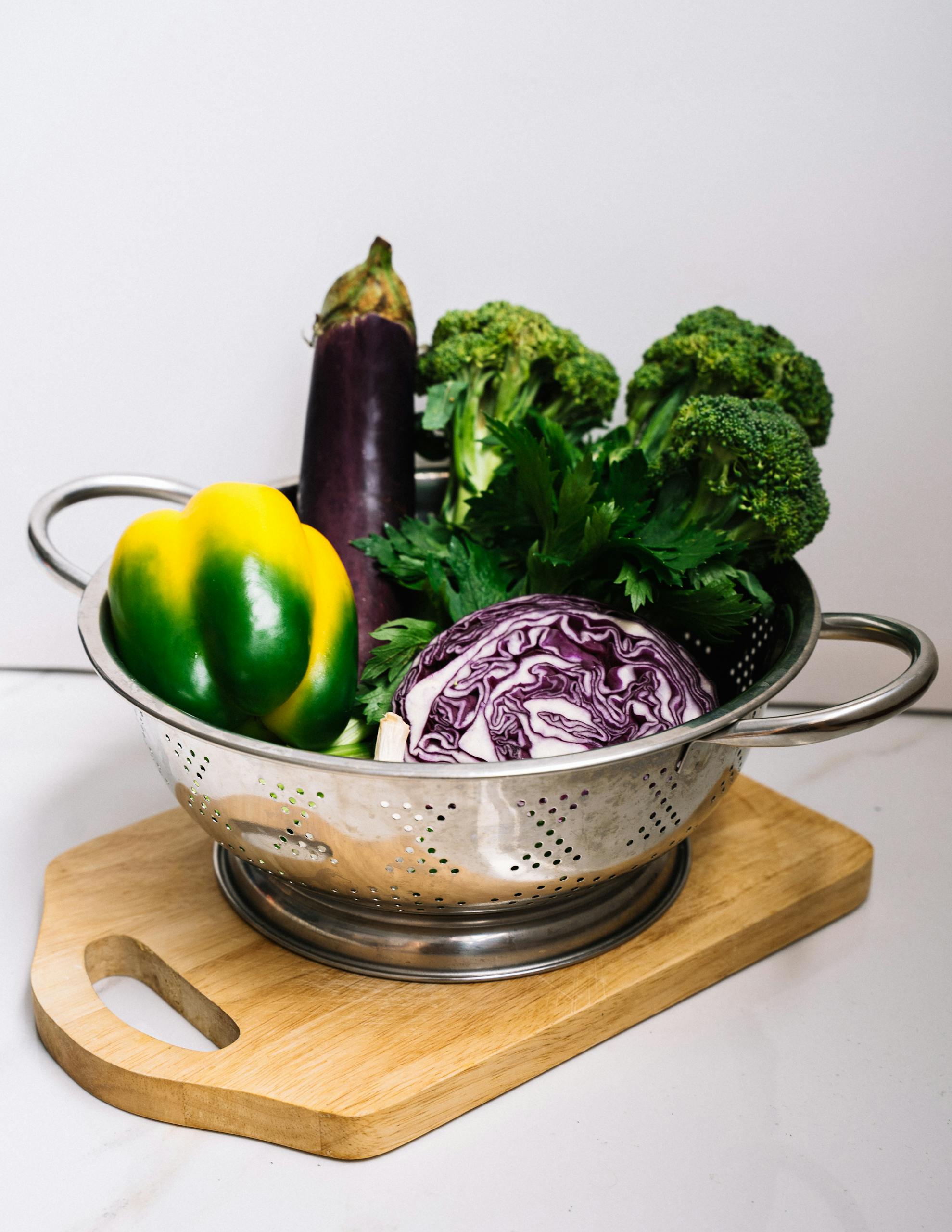 How to Make Meals Healthier: Vibrant fresh vegetables arranged in a steel strainer on a wooden cutting board, showcasing healthy eating and kitchen preparation.