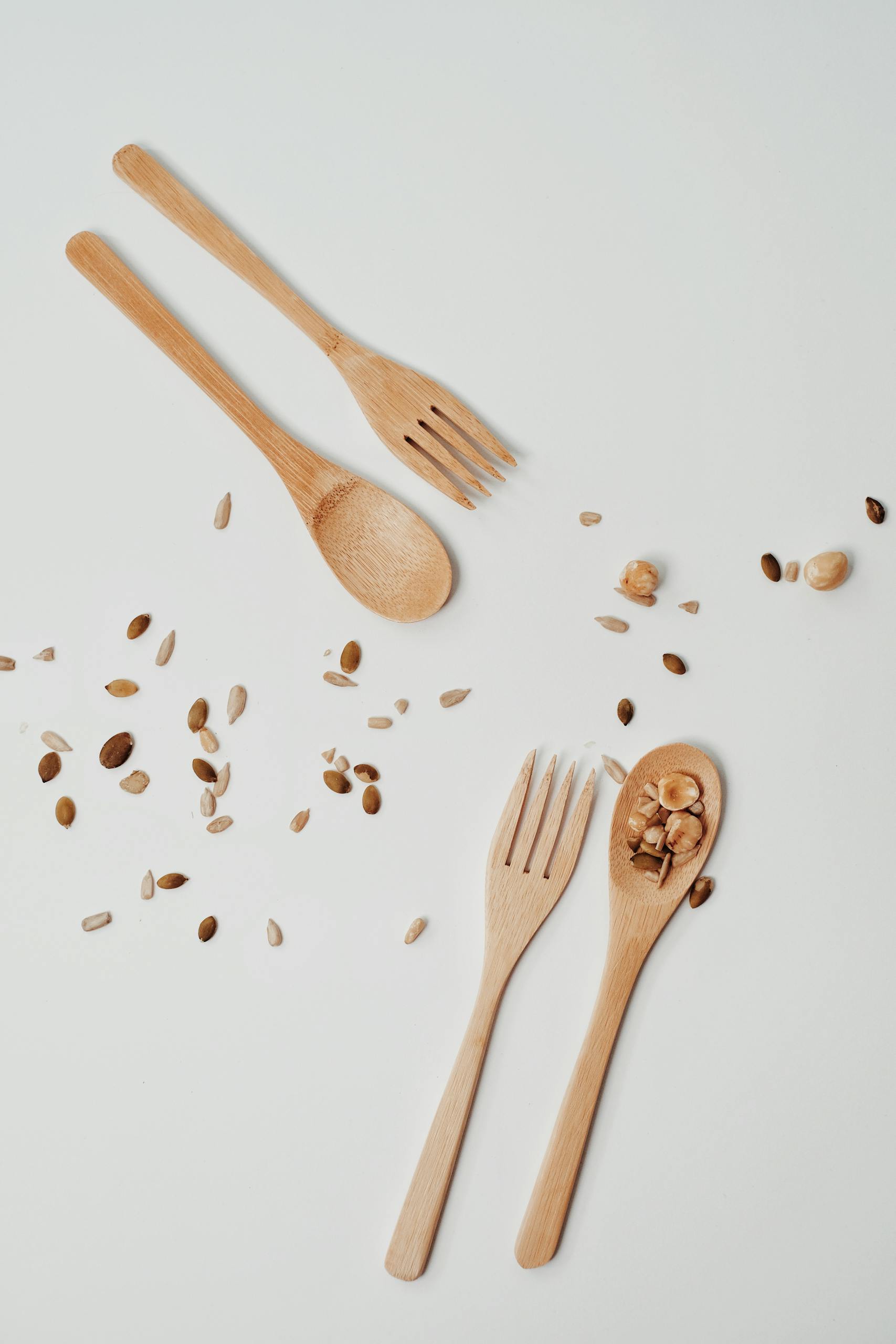How to Make Meals Healthier: Wooden forks and spoons with scattered seeds on a white background, showcasing sustainable dining.