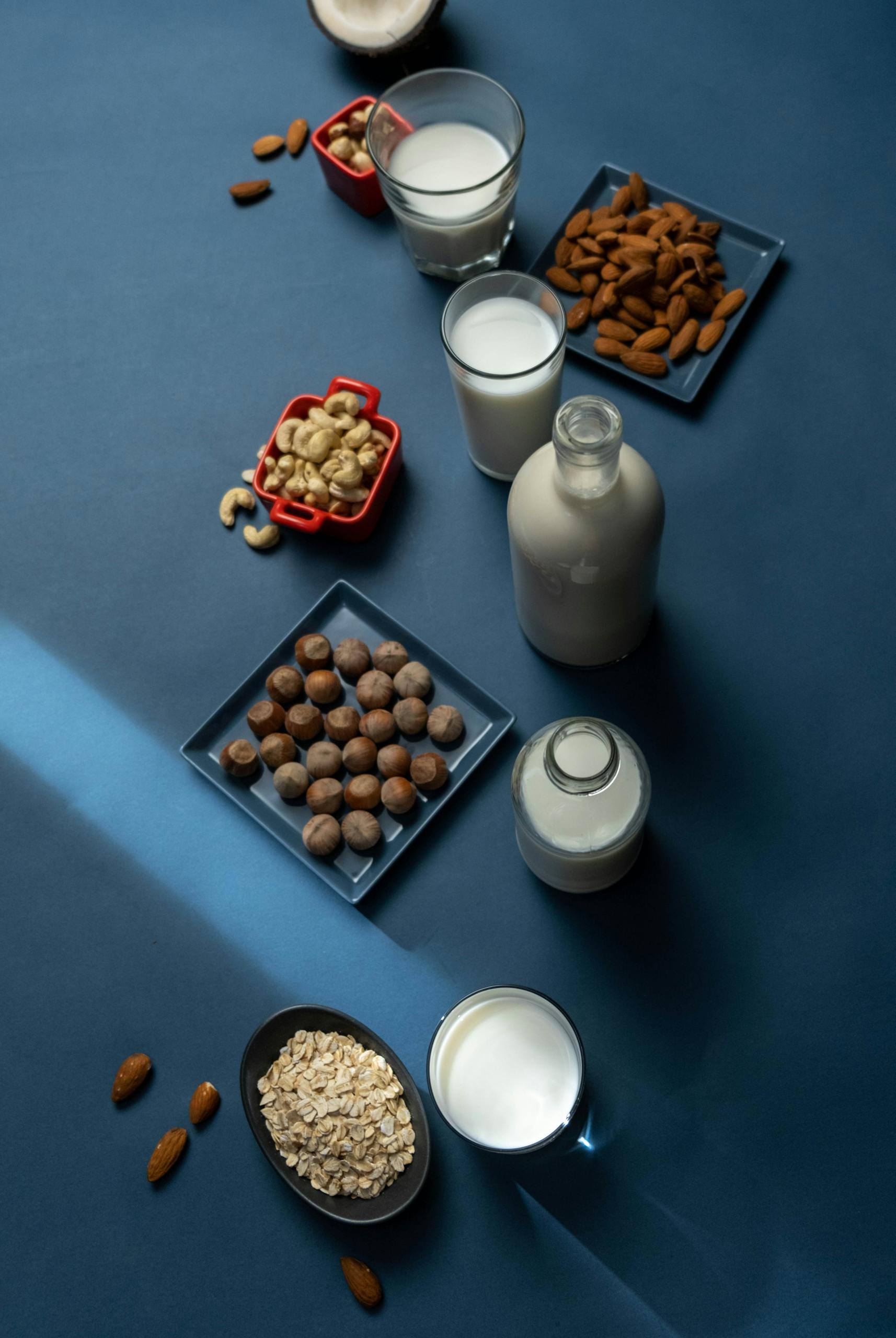 oat milk vs. almond milk vs. soy milk: A collection of nut milk and their ingredients arranged artistically on a blue background.