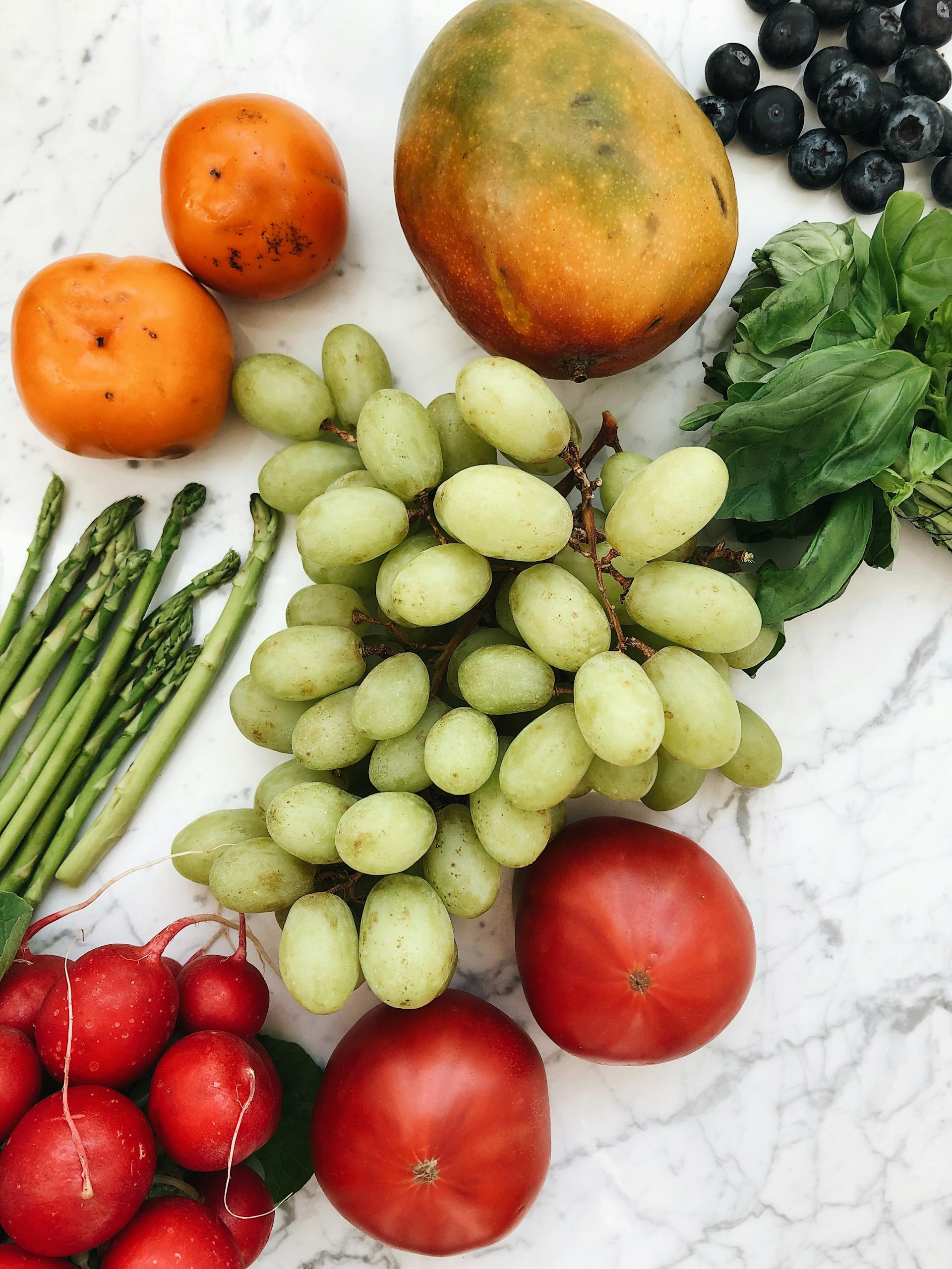 how to eat more whole foods: A vibrant mix of fresh fruits and vegetables including grapes, mango, and tomatoes on a marble surface.