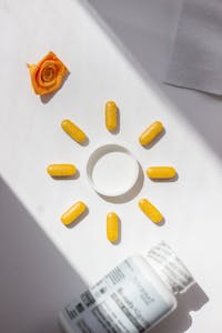 do you need vitamin D supplements: Bright yellow vitamin pills arranged in a sun shape with bottle and rose accent on white background.
