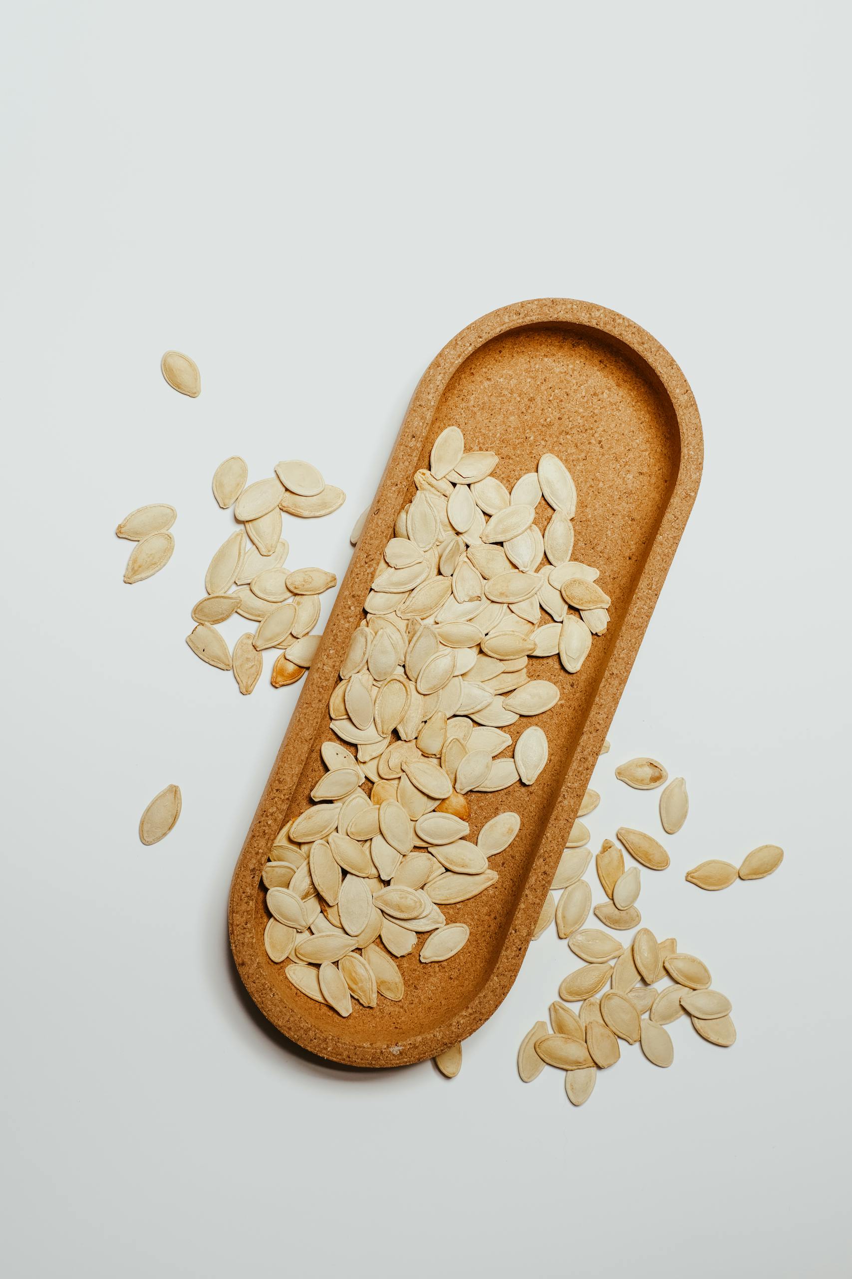 seed cycling for hormones: Close-up of raw organic pumpkin seeds on a wooden tray with a minimalist aesthetic.