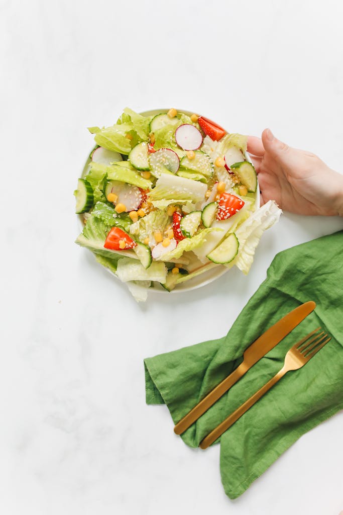 Volume Eating for Weight Loss: Colorful salad with fresh vegetables and golden cutlery on a green napkin, minimalist setup.