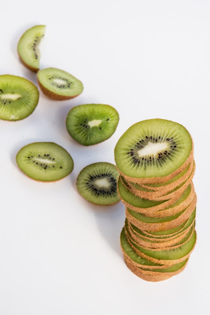 benefits of kiwi: Fresh kiwi slices stacked and scattered on a stark white background.