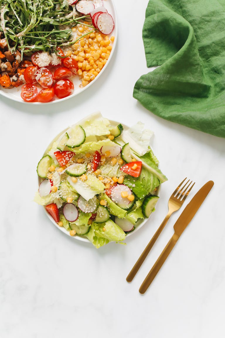 How to Lose Weight Without Feeling Hungry: Healthy and colorful vegetarian salad with gold cutlery on white background, perfect for a nutritious meal.