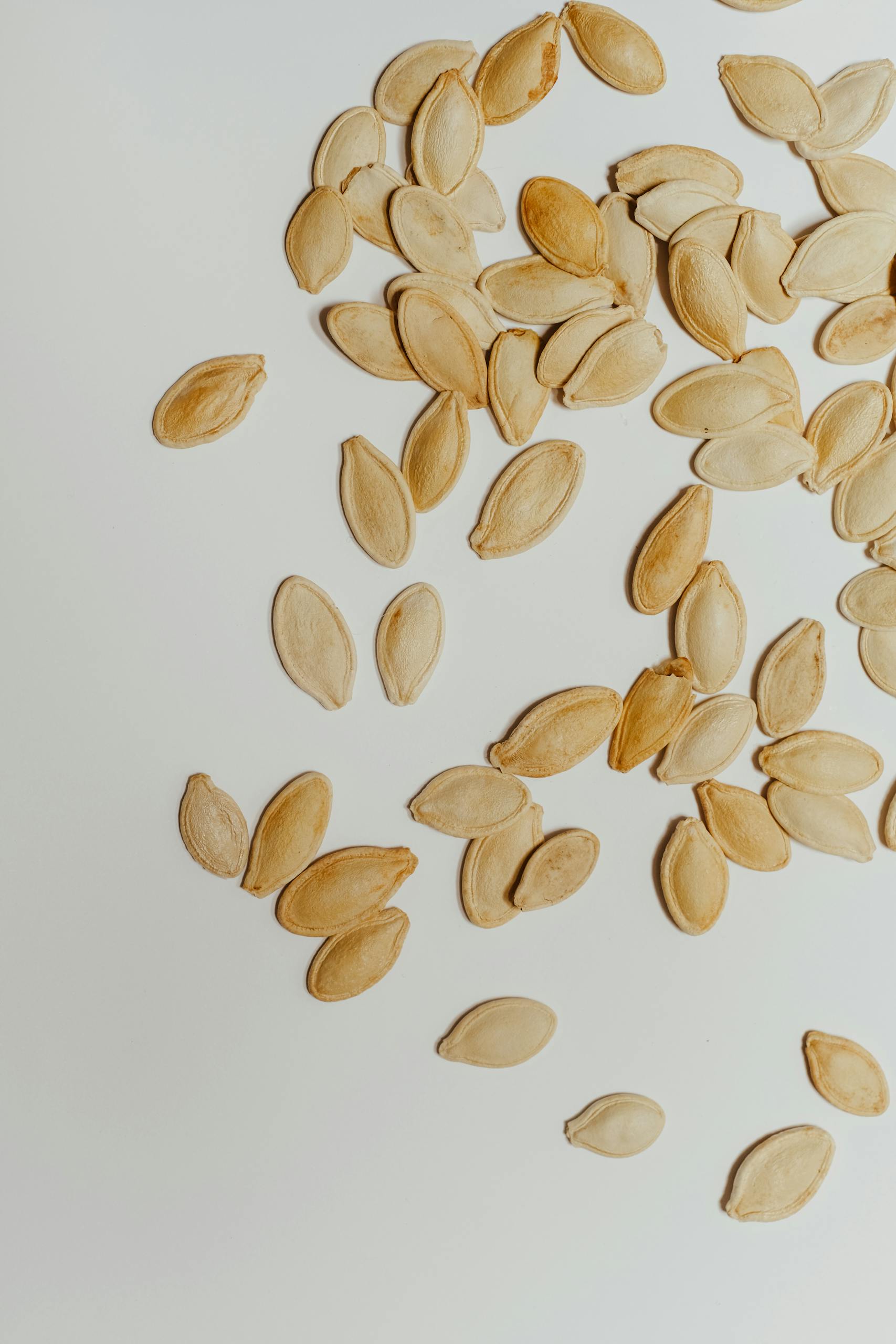 seed cycling for hormones: High-angle view of scattered raw pumpkin seeds on a white background, showcasing minimalist design.
